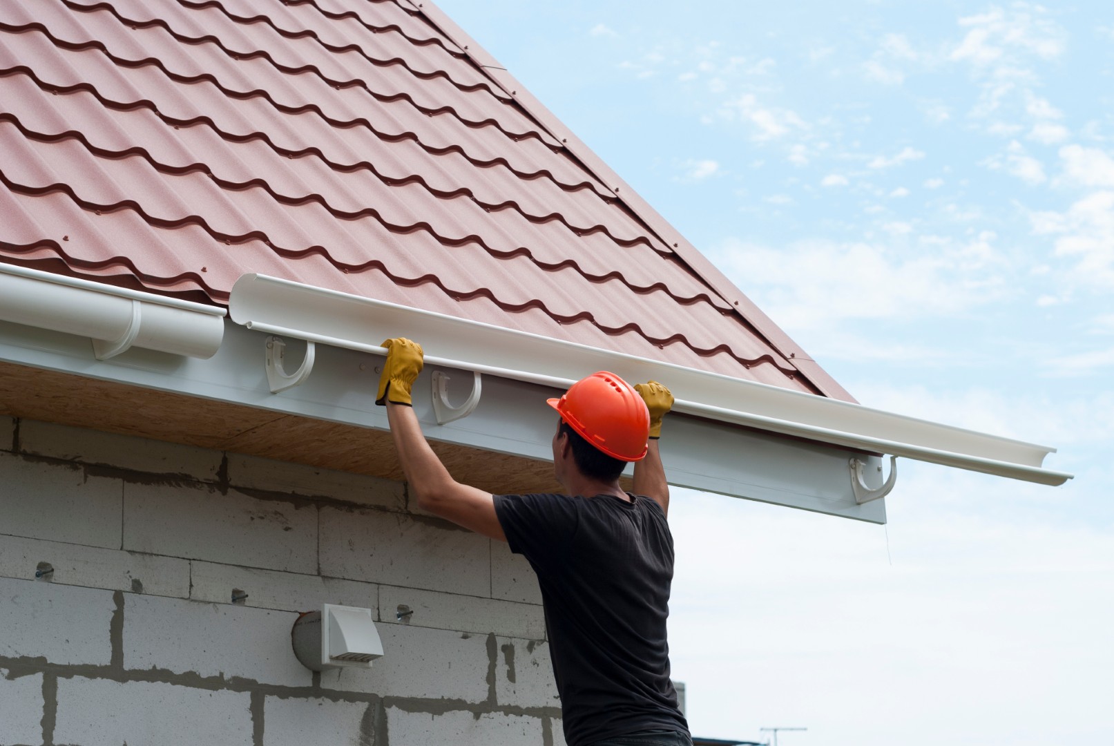 worker installs the gutter system on the roof